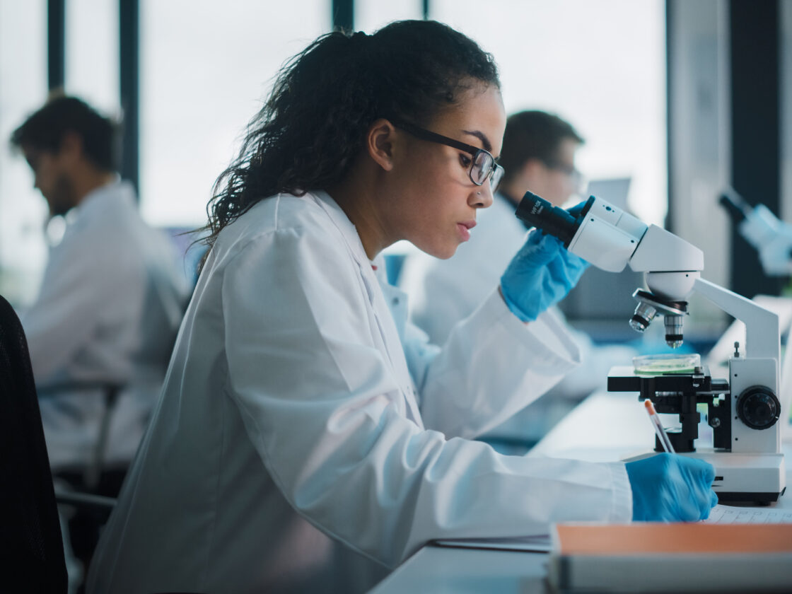 female scientist taking notes while using microscope