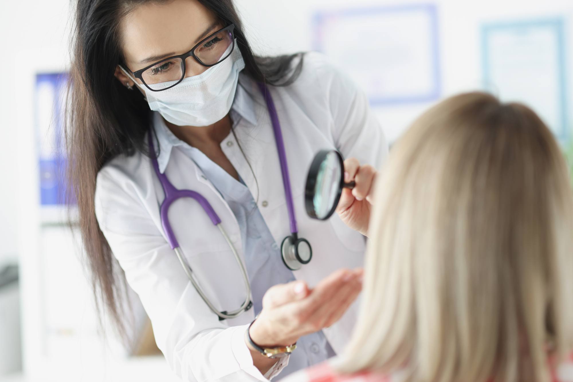 Doctor examining skin on patients face using magnifying glass