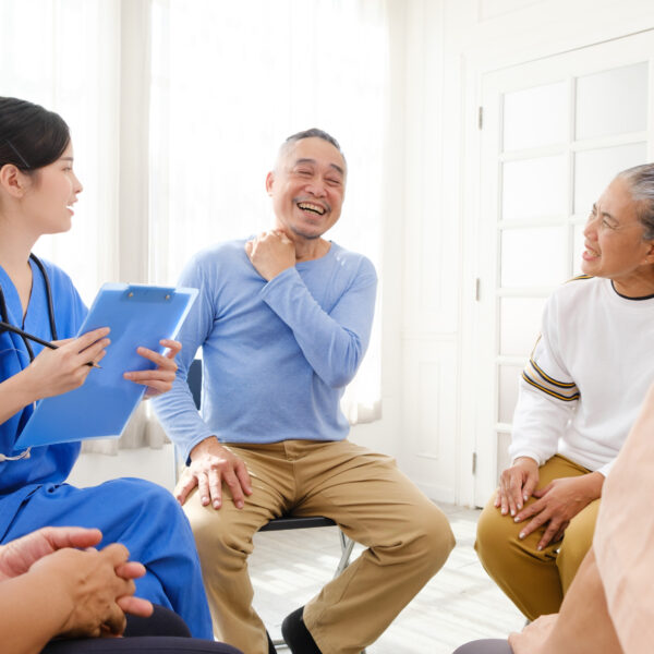 The caregiver therapist sits with a group of Asian senior people in a therapy session