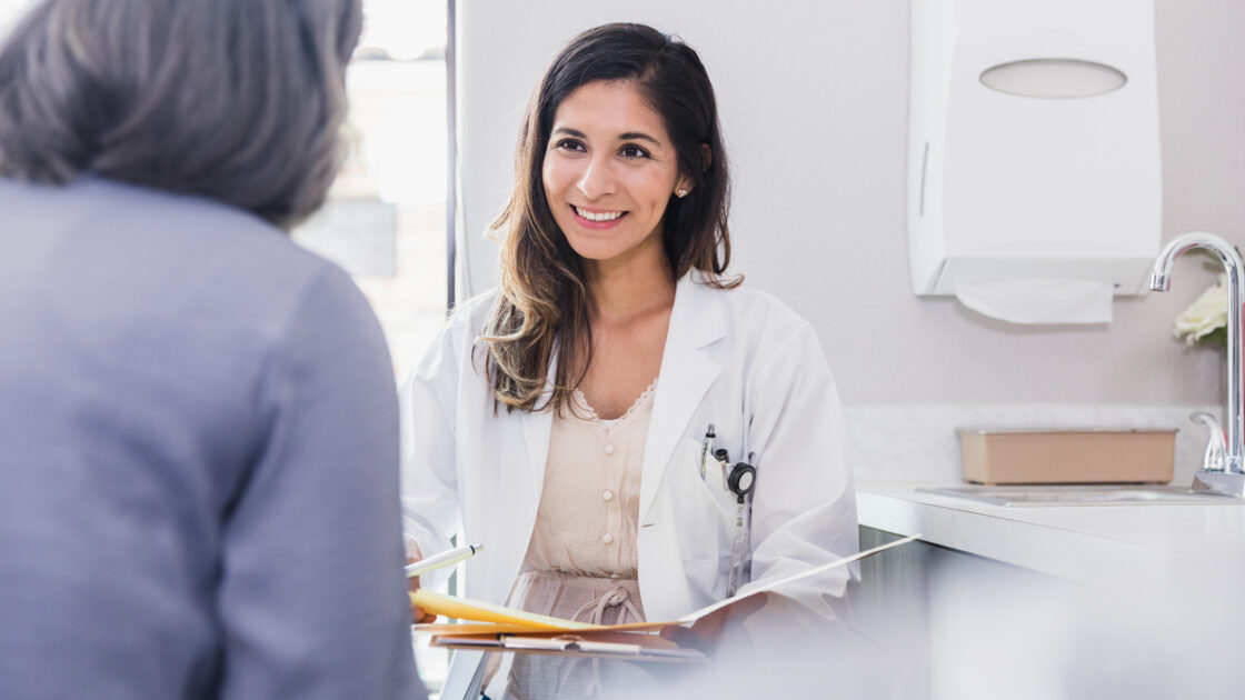 Cheerful and attentive female doctor smiles while listening to a female patient discuss her health during an annual medical exam.