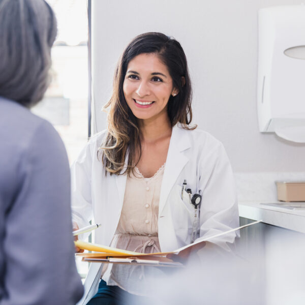 Cheerful and attentive female doctor smiles while listening to a female patient discuss her health during an annual medical exam.