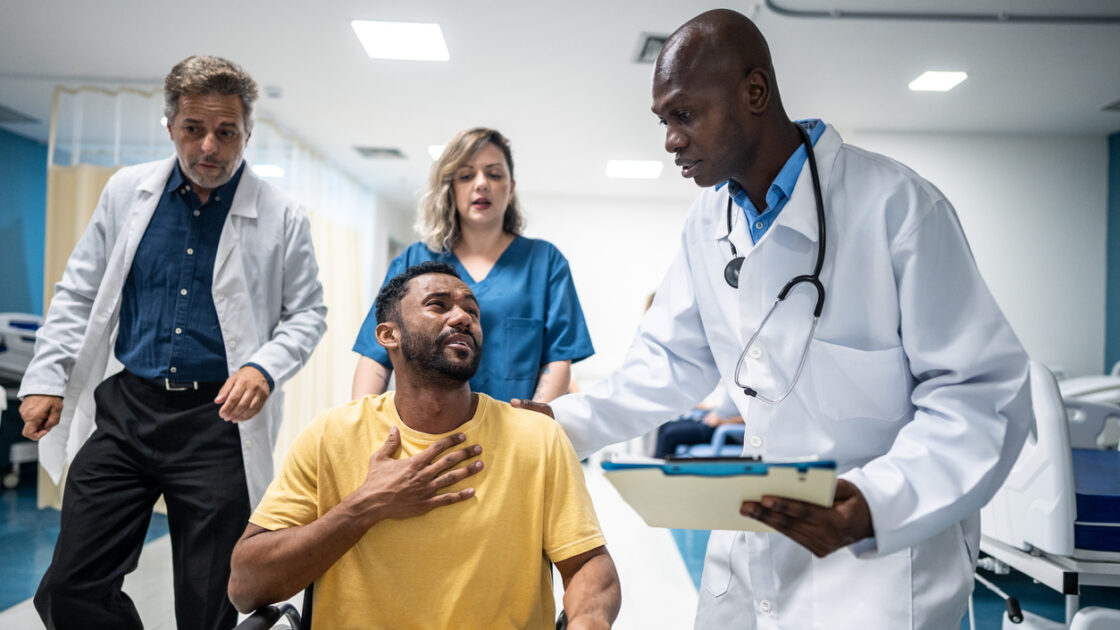 Nurse pushing patient in a wheelchair while doctor talks to him in the hospital